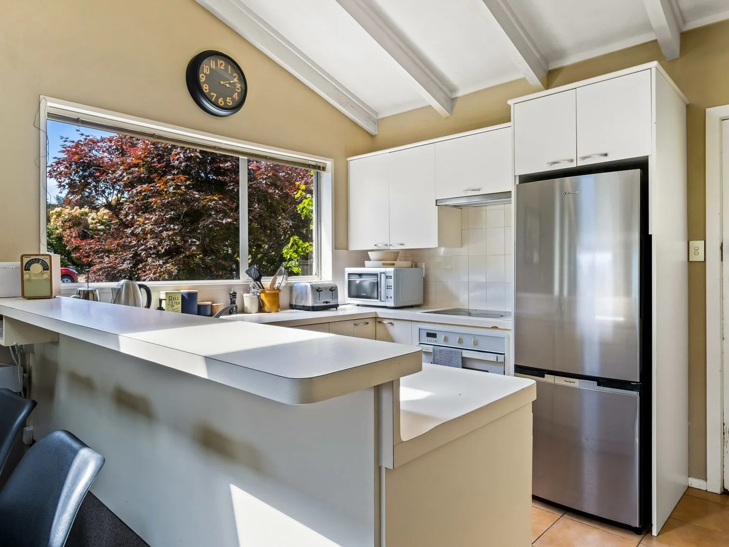 Una cocina luminosa con muebles blancos, un refrigerador de acero inoxidable y una ventana grande.