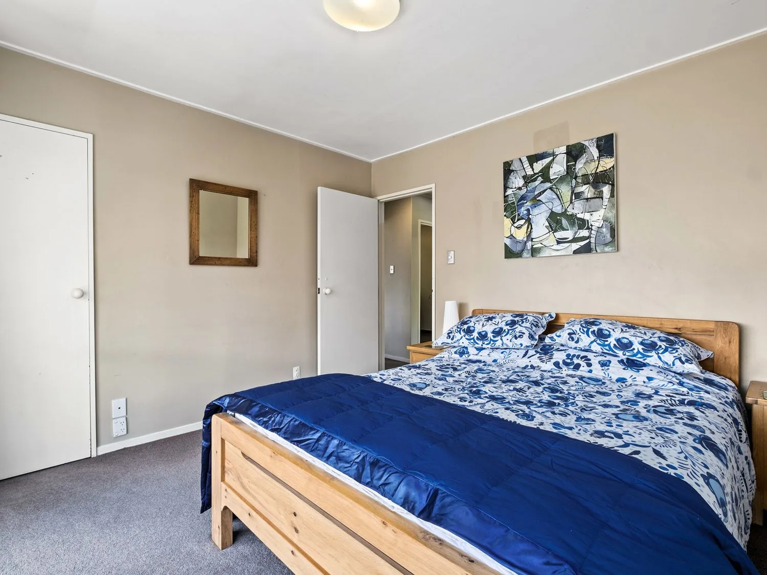 Un dormitorio con una cama de madera con ropa de cama azul y blanca, un espejo de pared y un cuadro abstracto en Taha Wai - Wanaka Holiday Home, en Wanaka.