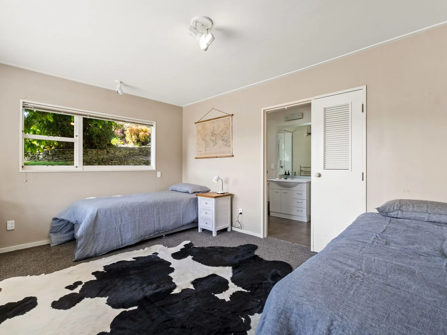 Un dormitorio con dos camas individuales, una mesa de noche y una alfombra con un diseño en blanco y negro en Taha Wai - Wanaka Holiday Home, en Wanaka.