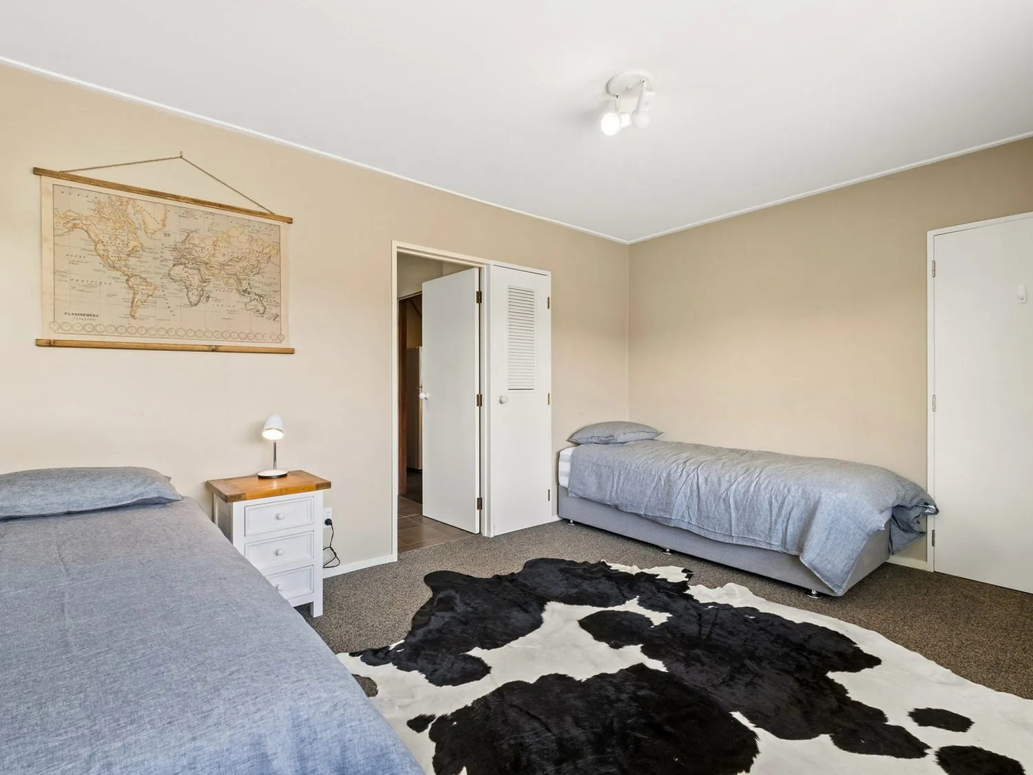 Un dormitorio con dos camas individuales, una mesa de noche con una lámpara, un mapamundi en la pared y una alfombra blanca y negra en el suelo en Taha Wai - Wanaka Holiday Home, en Wanaka.