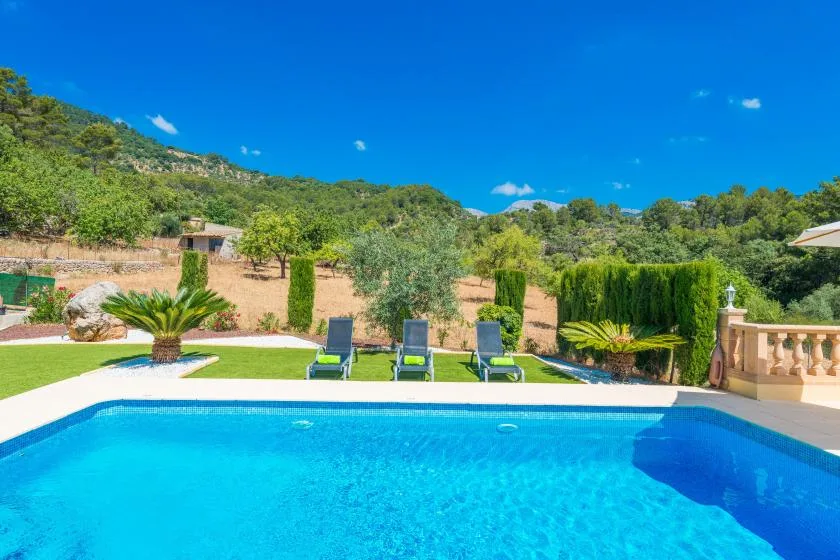 An outdoor swimming pool overlooks a landscaped garden and green hills.