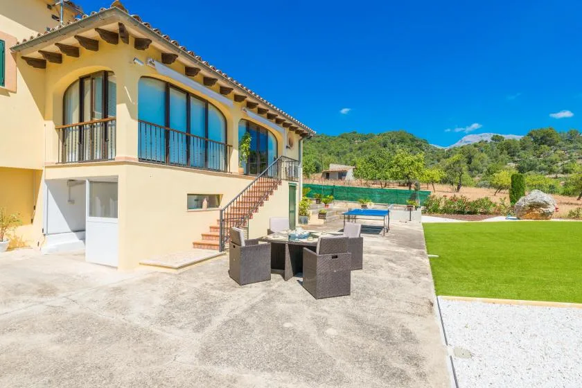 A house patio with outdoor seating beside a green lawn and distant hills.