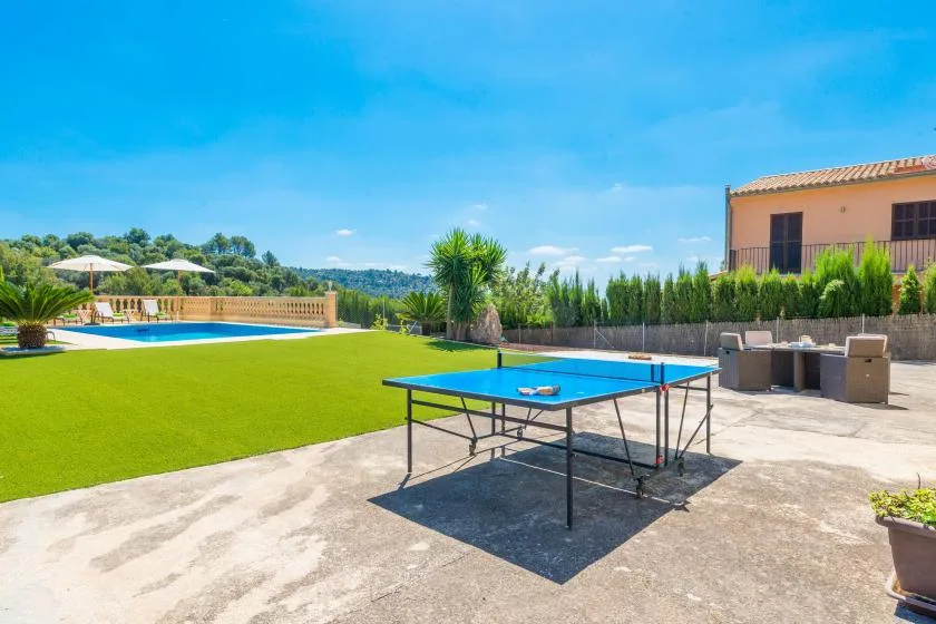 Outdoor recreation area with a table tennis table beside a lawn and swimming pool.