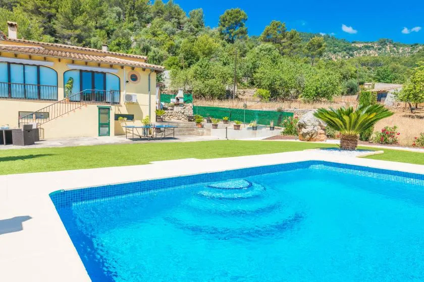 An outdoor swimming pool sits beside a villa and landscaped garden.