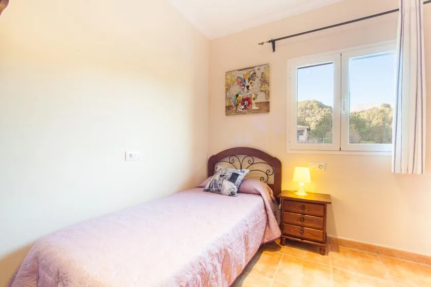 A bedroom with a bed beside a window and a small bedside table.