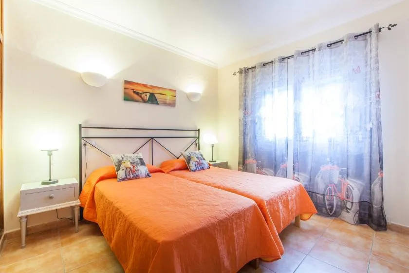 A bedroom with two beds covered in orange bedspreads and a curtained window.