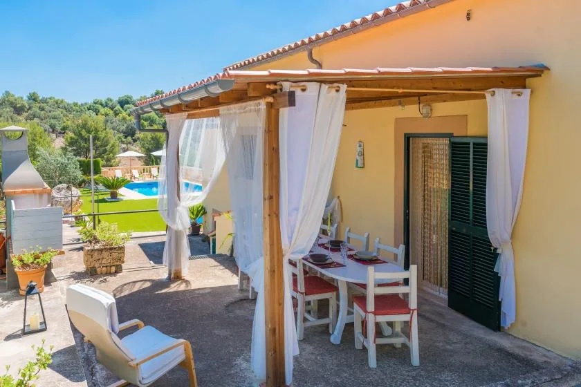 A shaded outdoor dining area with white curtains and a table beside the house.