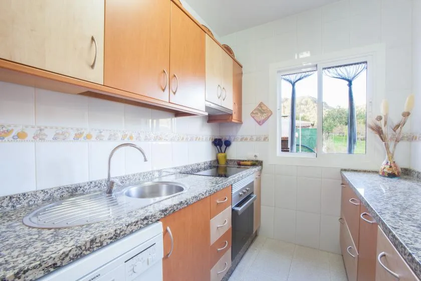 A bright kitchen with wooden cabinets, a sink, and a window overlooking greenery.