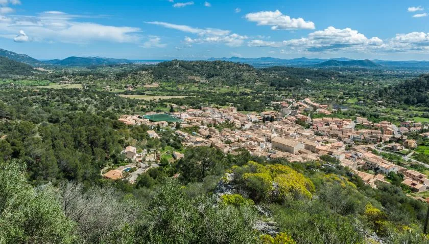 Aerial view of a town amid green hills beneath a blue, cloudy sky.