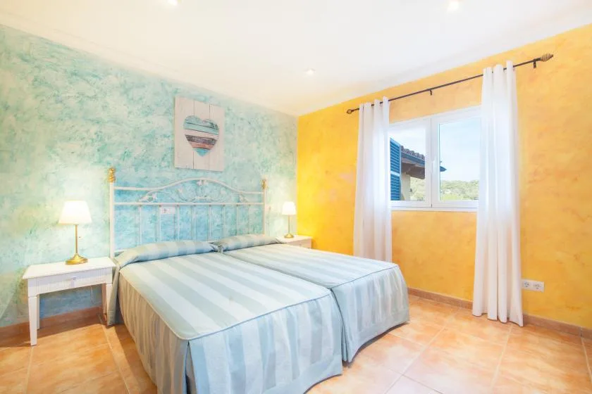 A bright bedroom with two beds, bedside tables, and a large window.