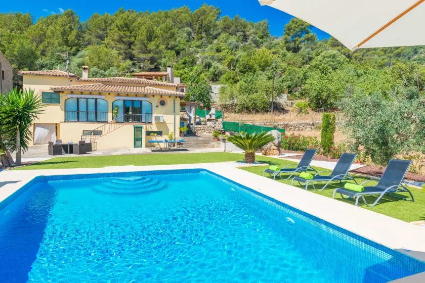 An outdoor swimming pool sits beside a house, with loungers on the lawn.