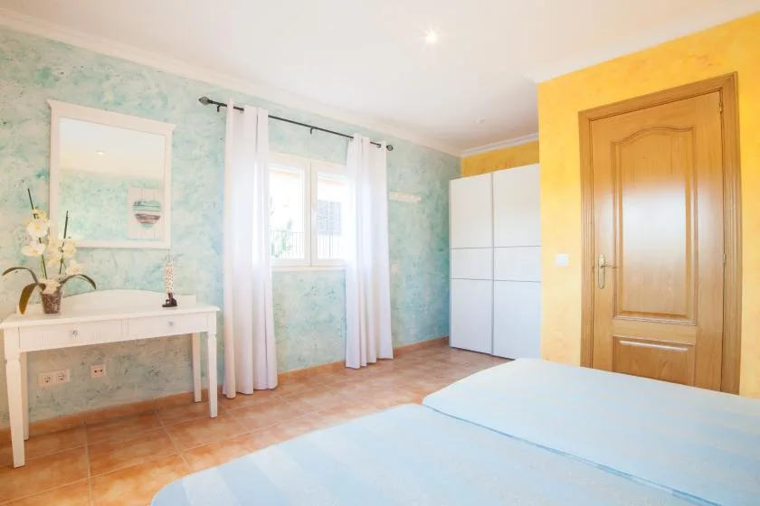 A bright bedroom with a bed, a window, and a white wardrobe.