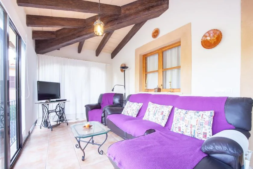A living room with purple seating, a television, and exposed wooden ceiling beams.