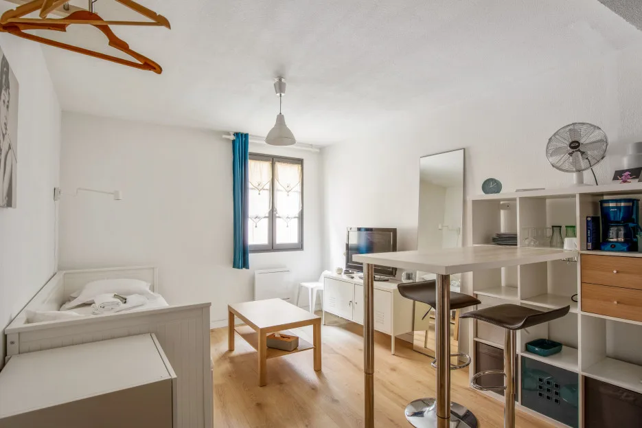 A bright room with a bed, a table, and shelving beside a window.