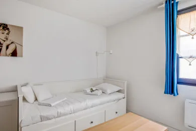 A bright bedroom with a white bed and blue curtains beside the window.