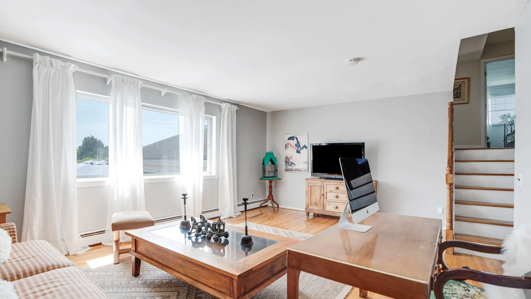 Una sala luminosa con grandes ventanas con cortinas y una mesa de centro de madera.