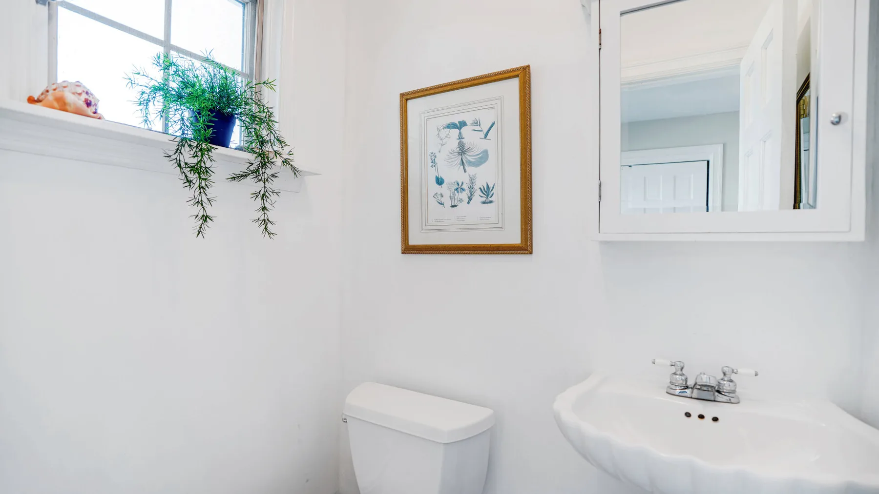 Un baño luminoso con un inodoro y un lavabo bajo un espejo de pared.