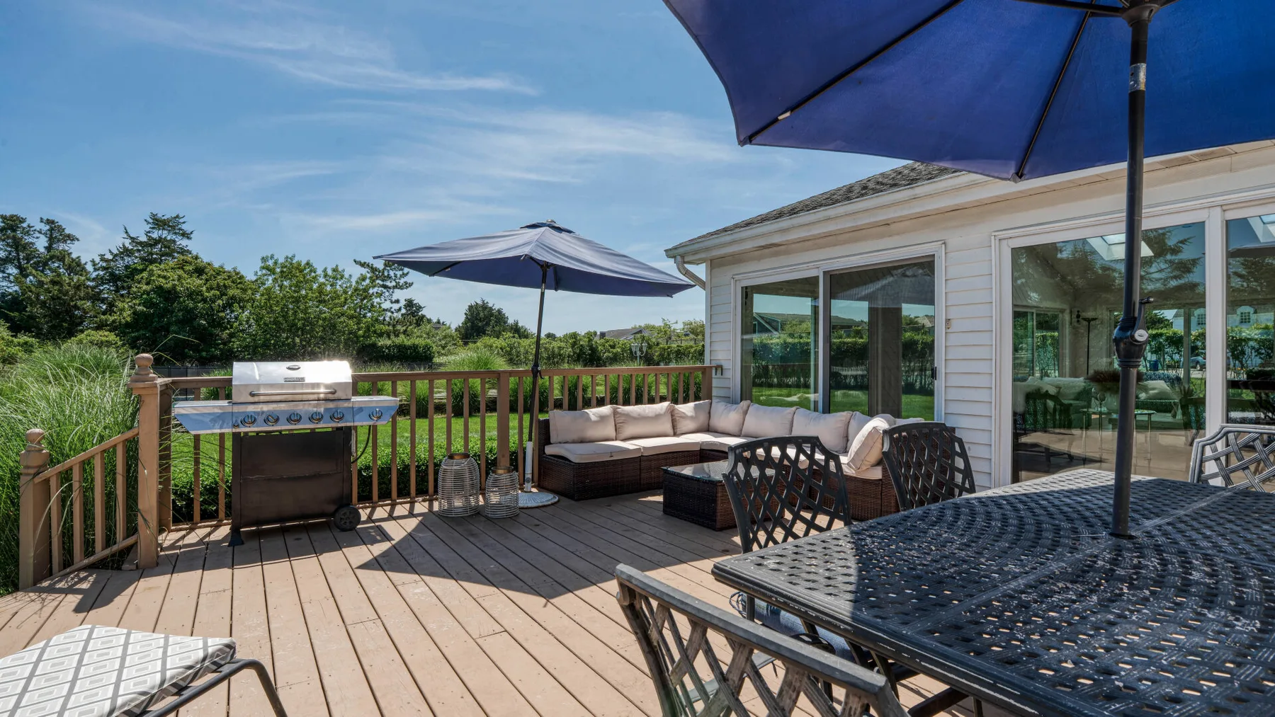A furnished outdoor deck beside a house, with seating and patio umbrellas.