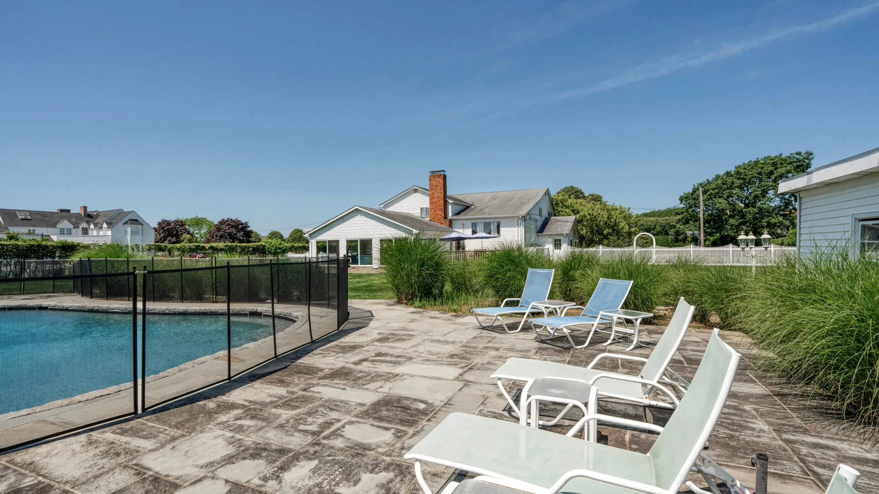 An outdoor swimming pool with loungers on the surrounding paved patio.