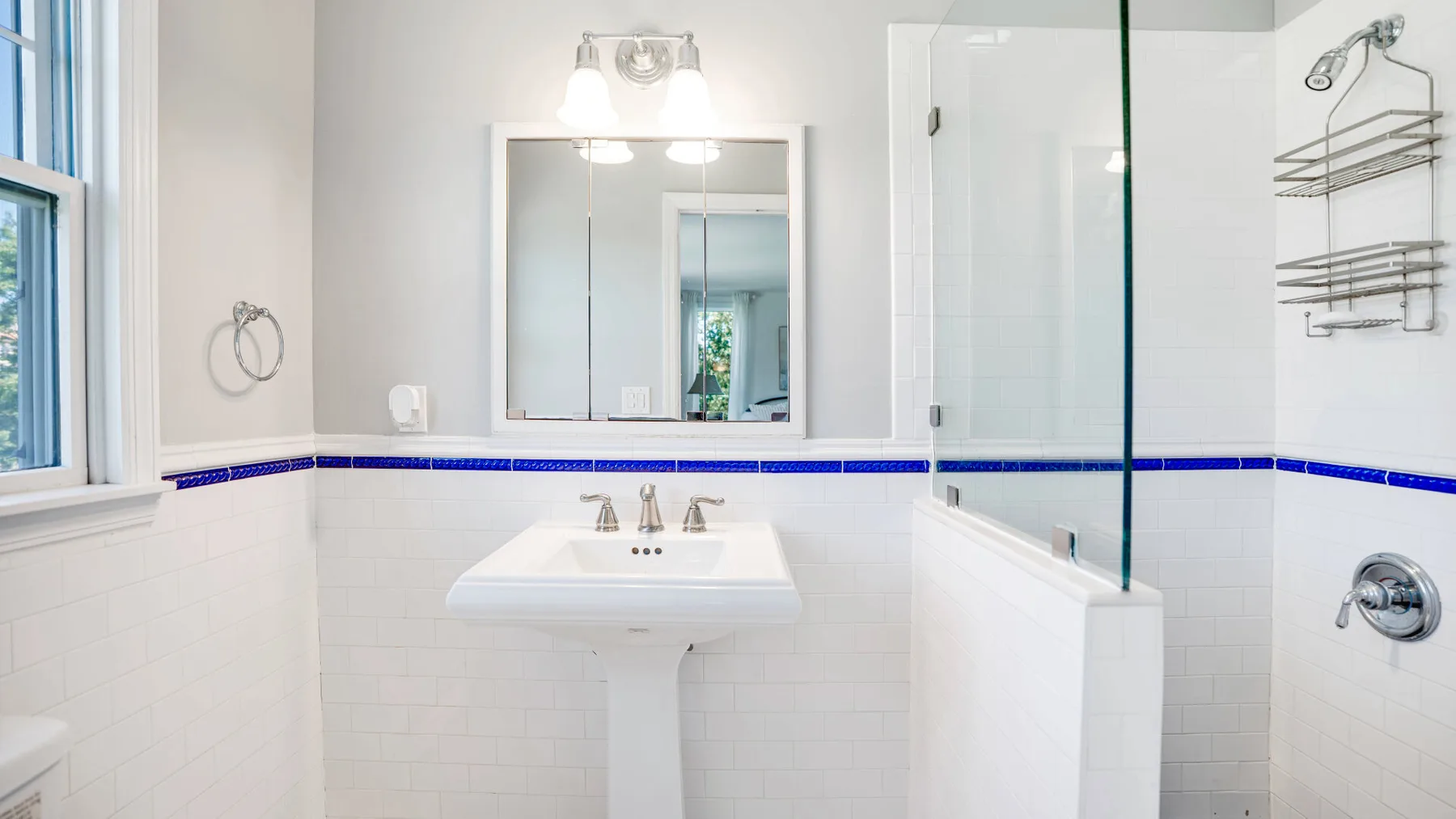 Un baño luminoso con lavabo blanco, espejo y mampara de ducha de vidrio.