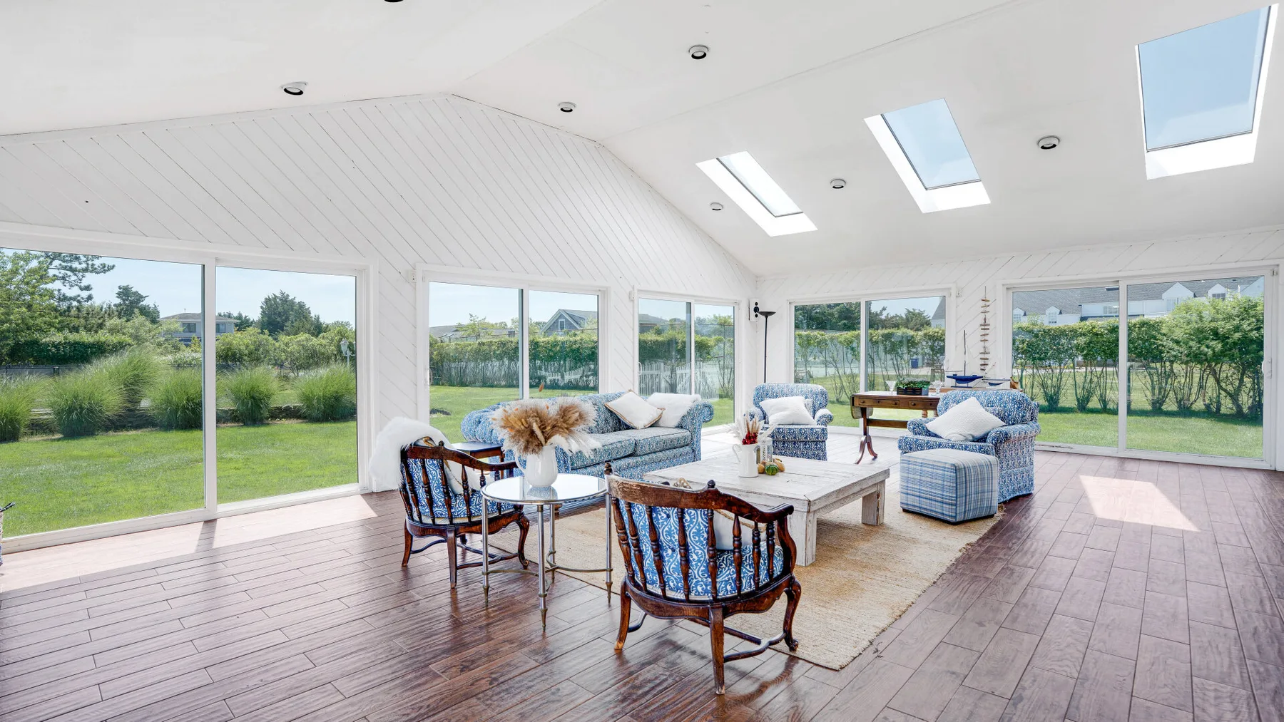A bright sunroom with wide windows, seating, and a coffee table.