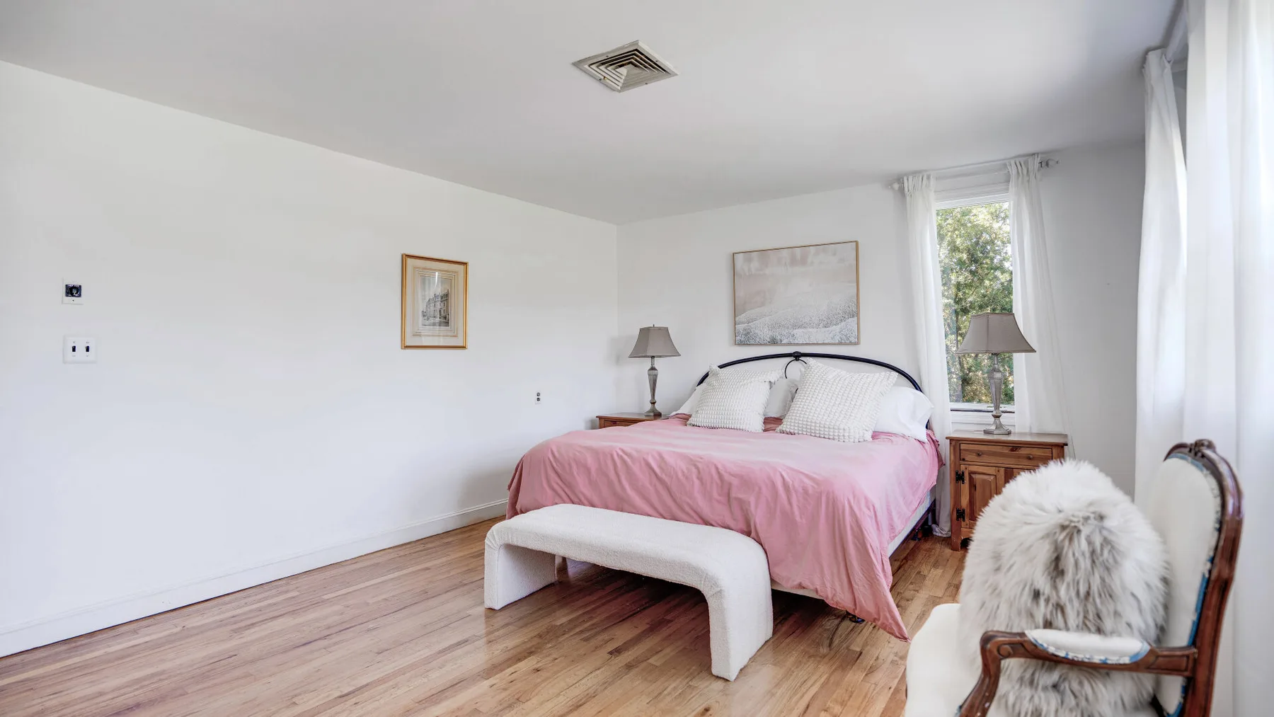Un dormitorio luminoso con una cama vestida de rosa junto a una ventana.