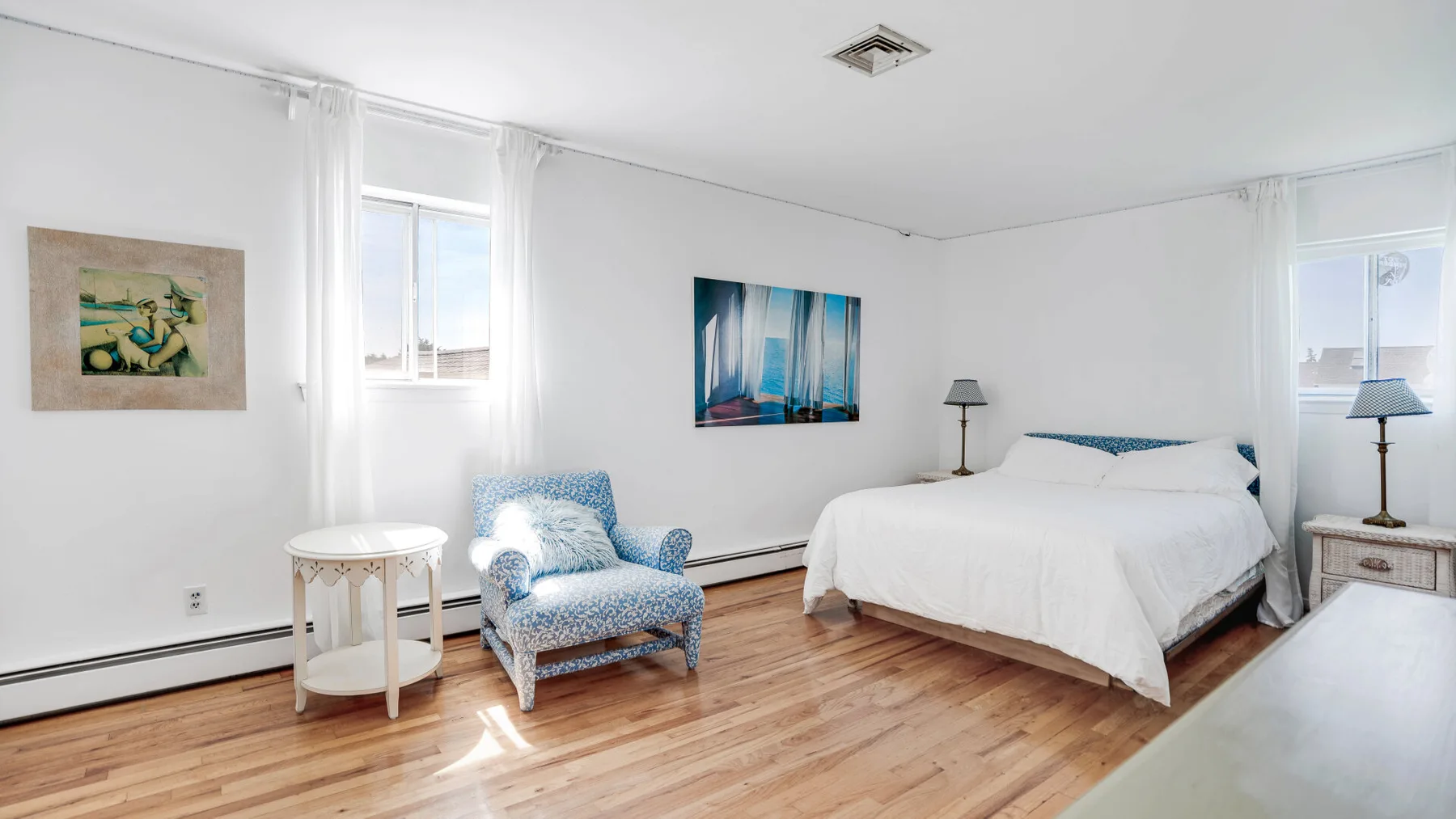Un dormitorio luminoso con una cama, asientos azules y ventanas grandes.