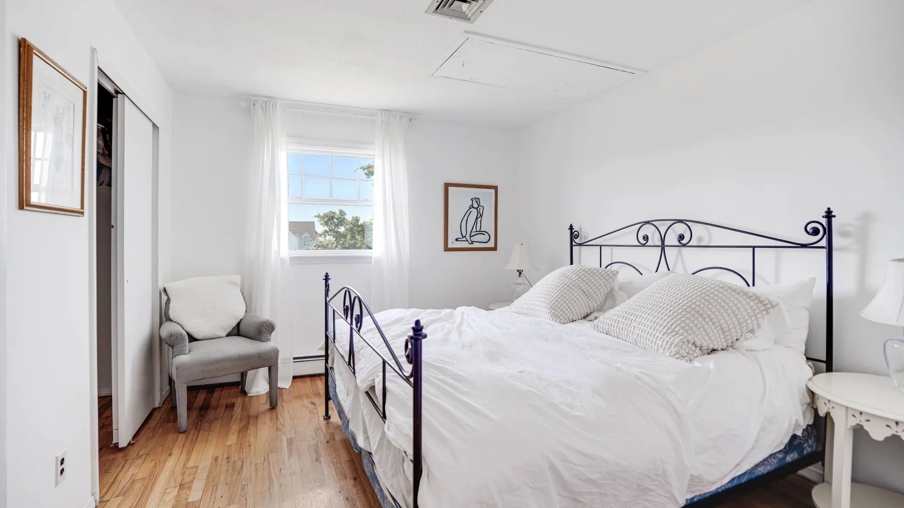 Un dormitorio luminoso con una cama de metal, ropa de cama blanca y una ventana.