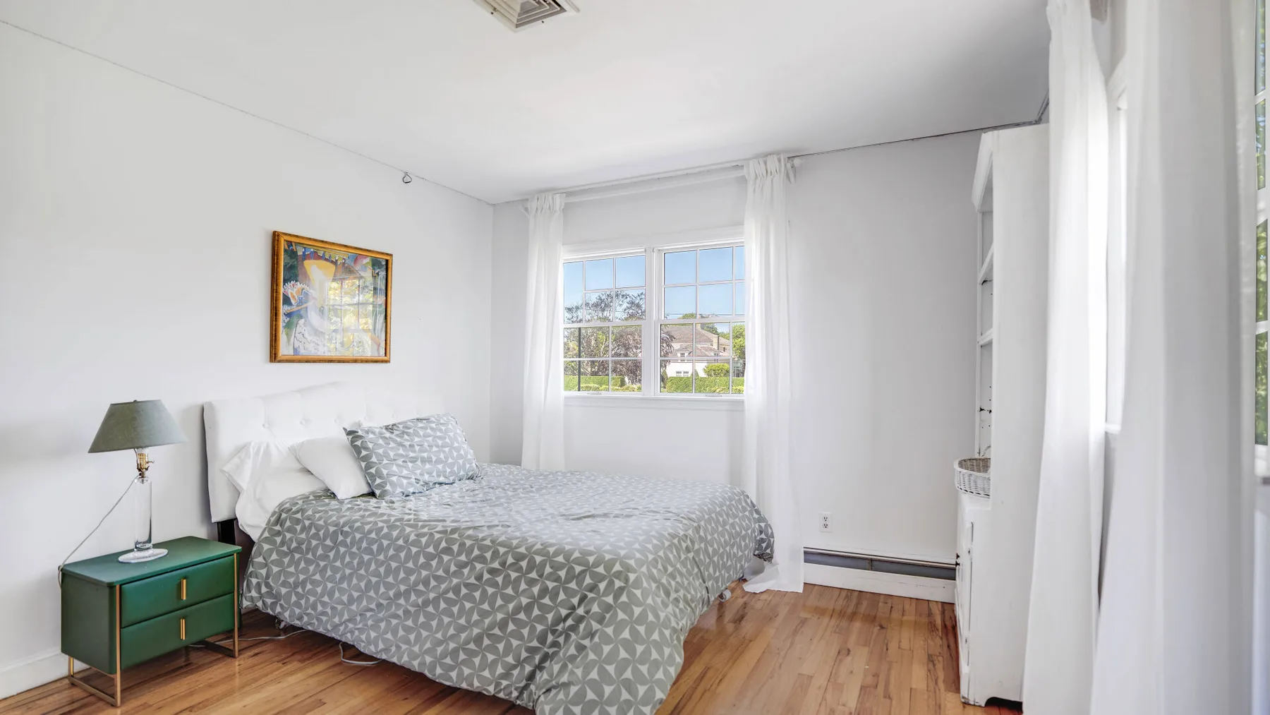 Un dormitorio con una cama tendida junto a una ventana luminosa.