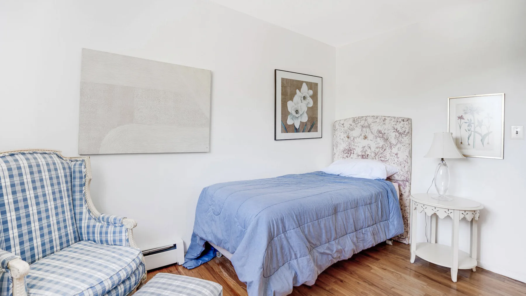Un dormitorio con una cama cubierta con ropa de cama azul y un sillón estampado.