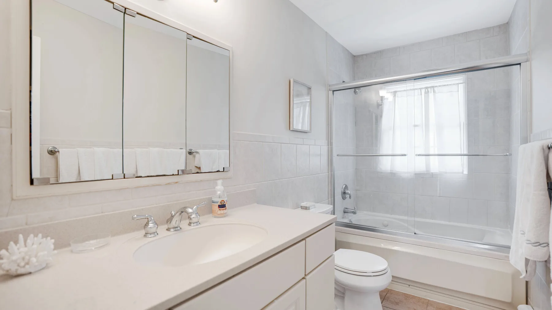 Un baño luminoso con un amplio tocador y una bañera detrás de una mampara de vidrio.