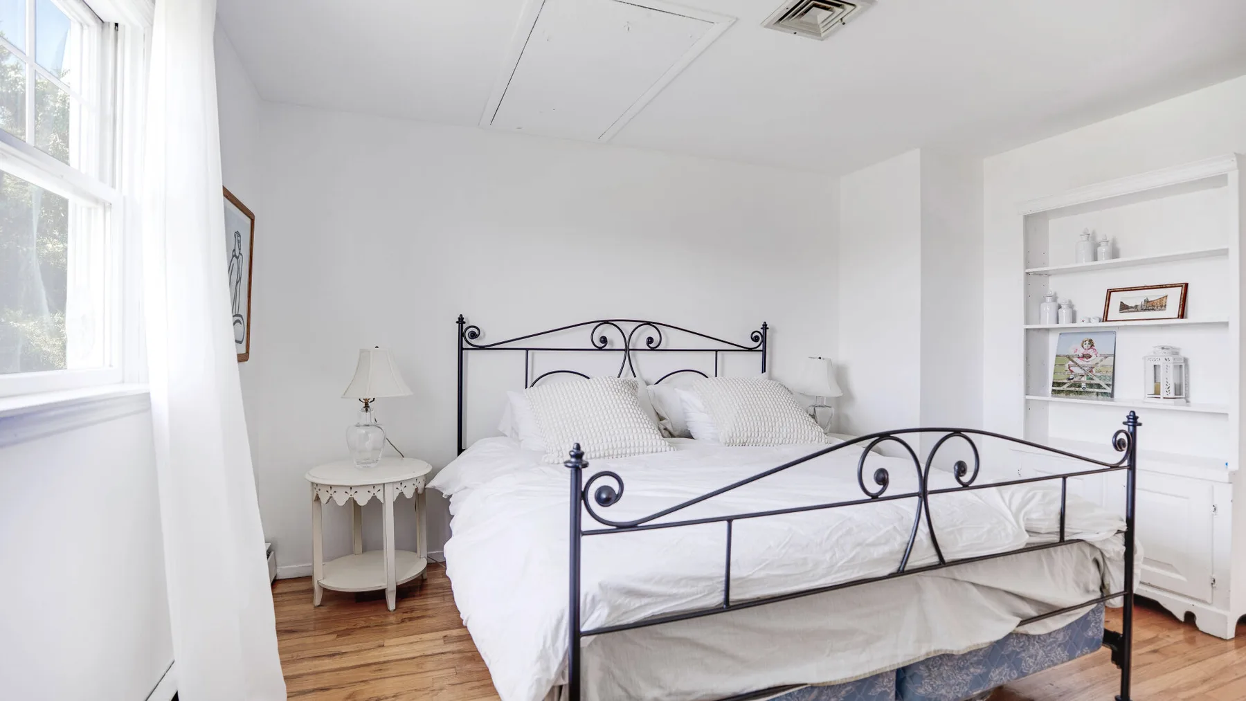 Un dormitorio luminoso con una cama blanca y una estantería empotrada.