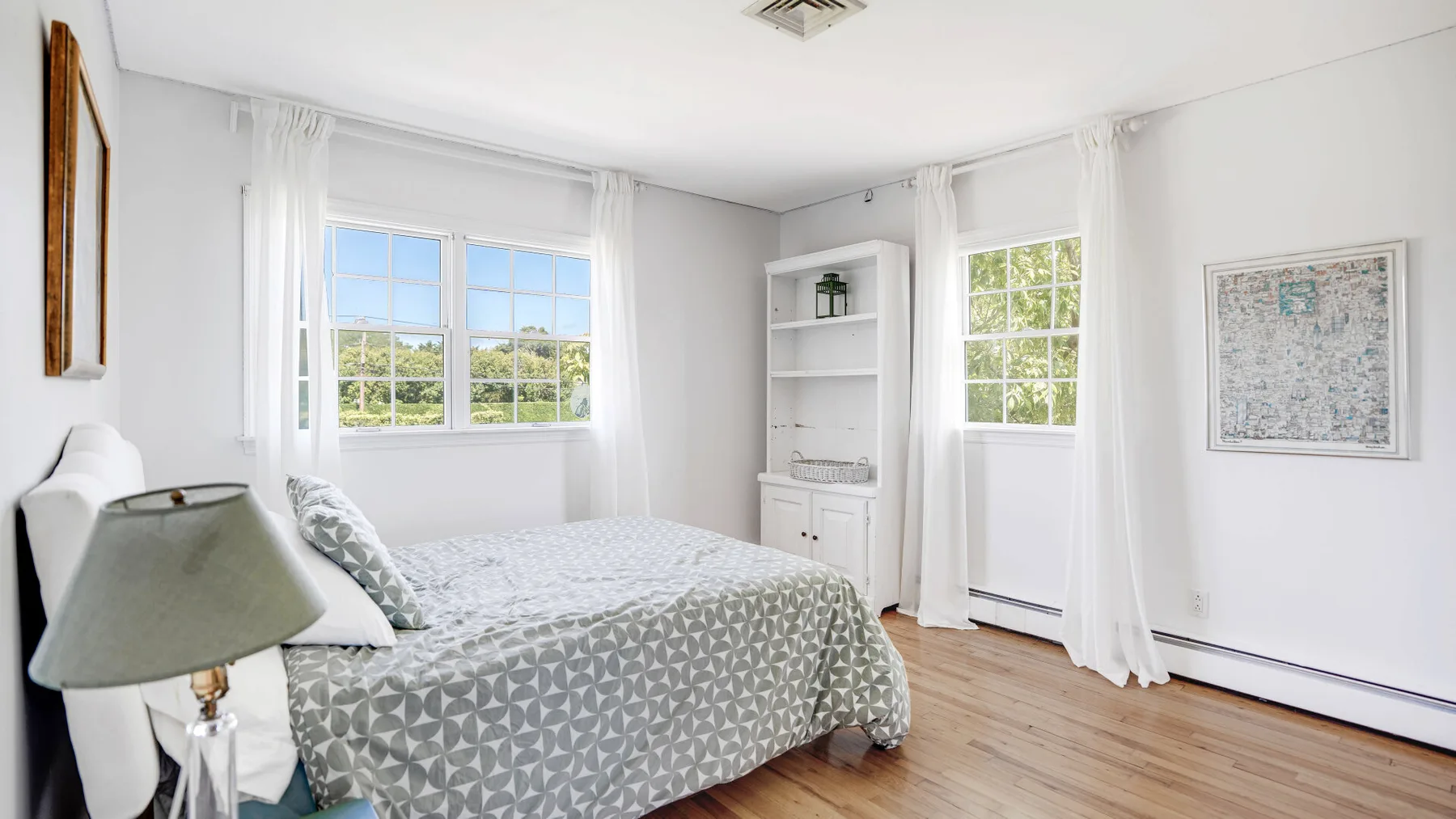 Un dormitorio luminoso con una cama, ventanas con cortinas y estanterías empotradas.