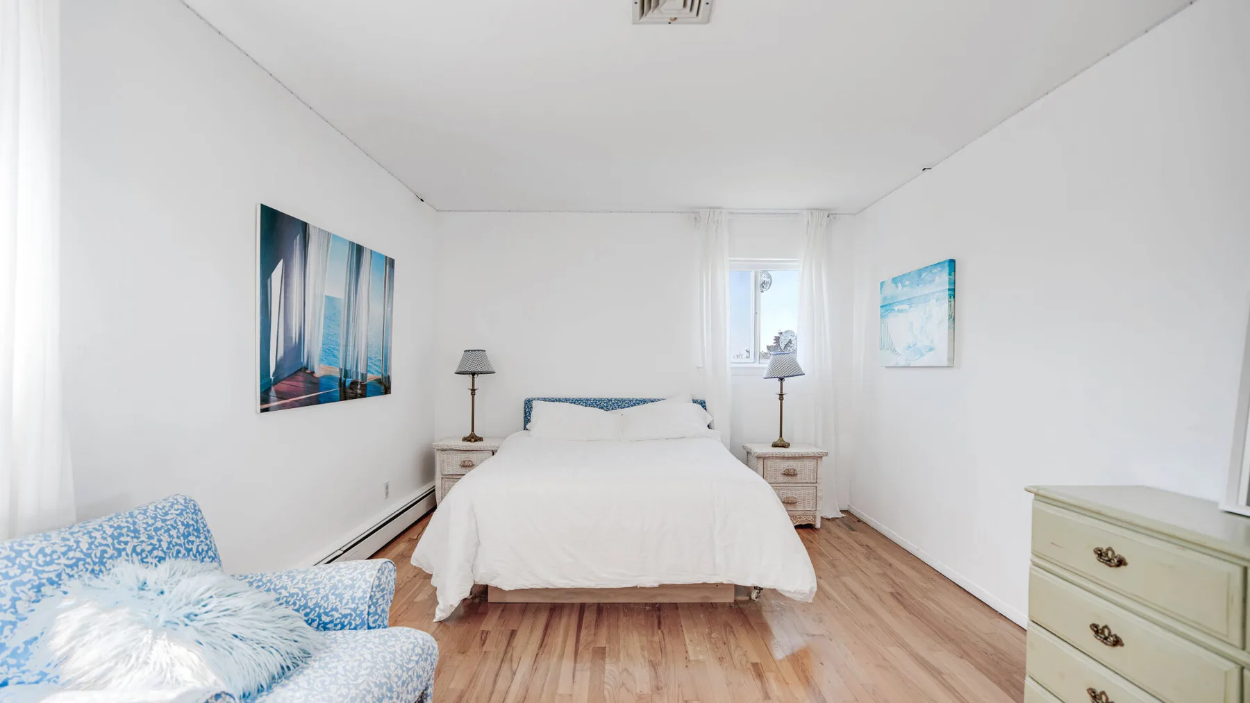 Un dormitorio luminoso con una cama, mesitas de noche y un sillón estampado.