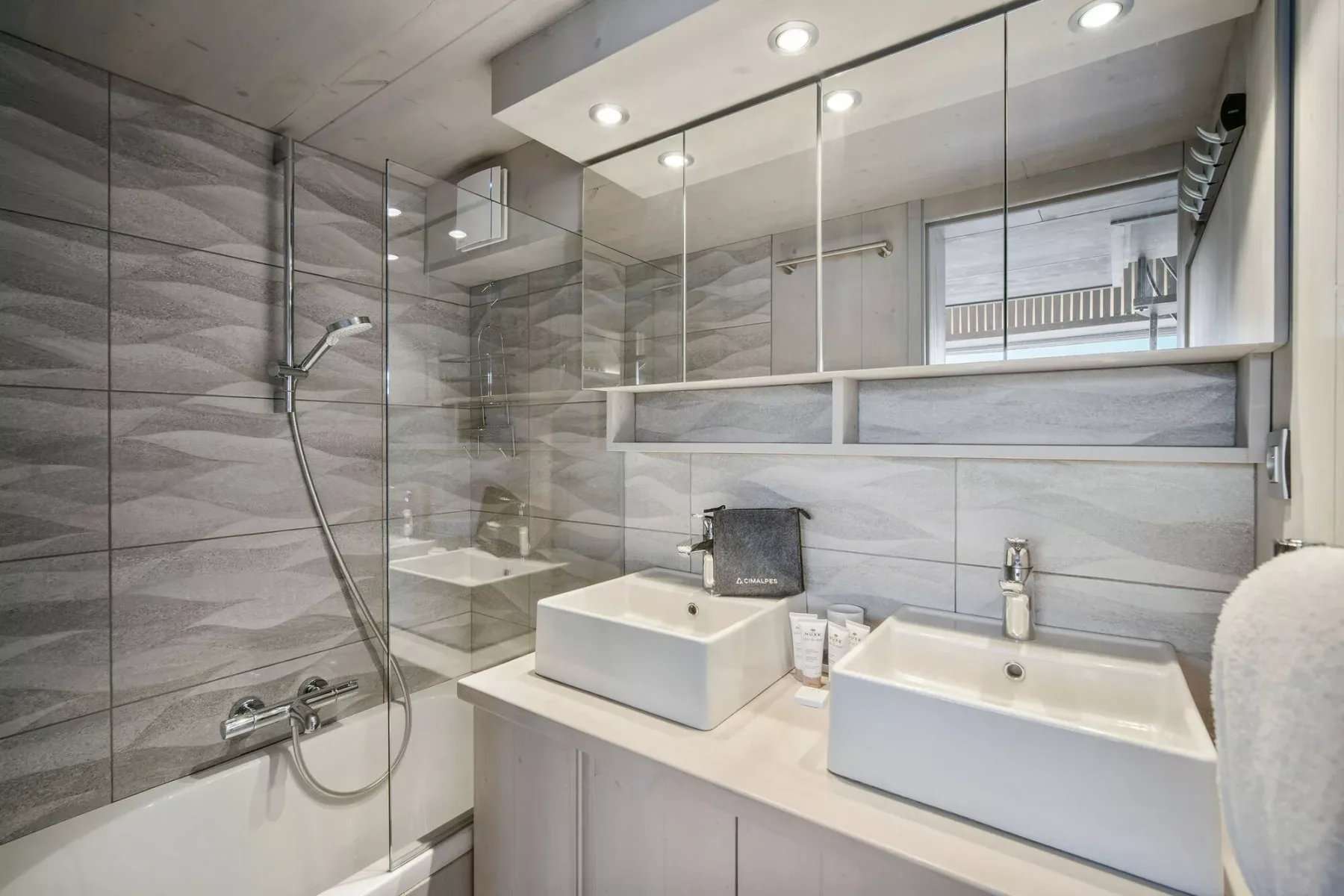 Un baño moderno con una ducha de vidrio y un tocador con dos lavabos.