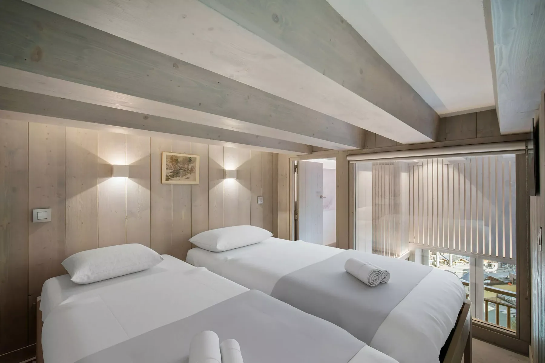 A bedroom with two beds beside a window with blinds.