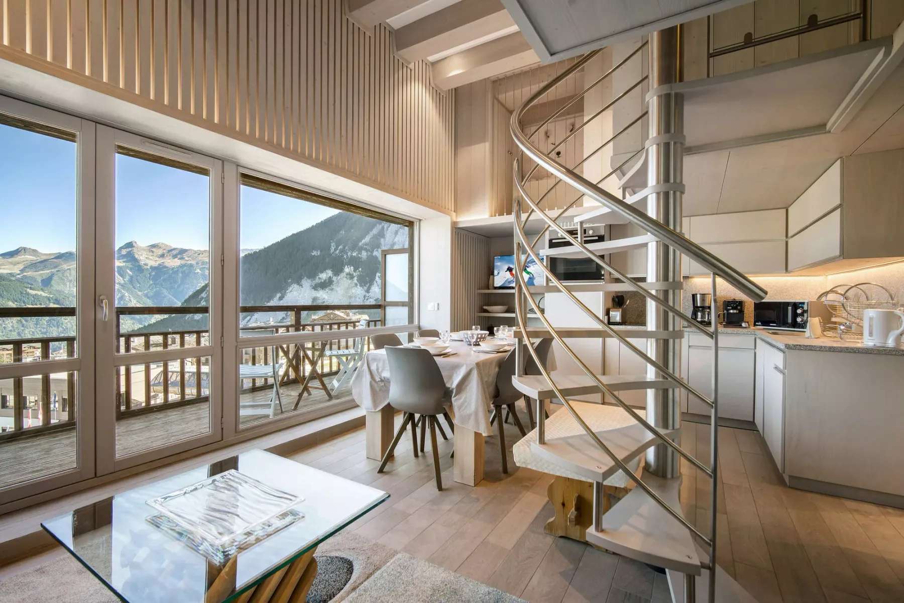 Un comedor y cocina luminosos se abren a un balcón con vistas a las montañas.
