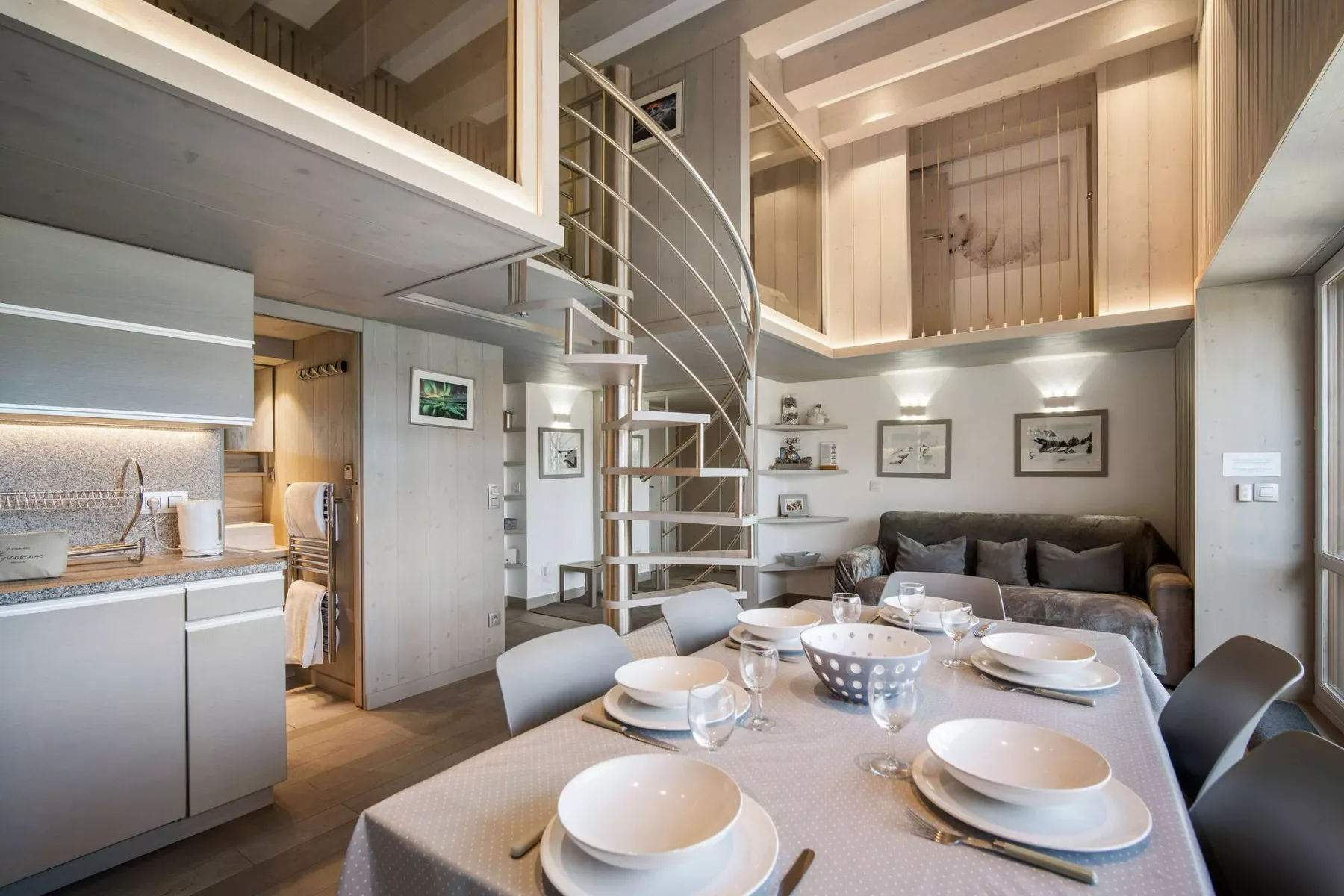 A dining area with a set table beside a living area and spiral staircase.