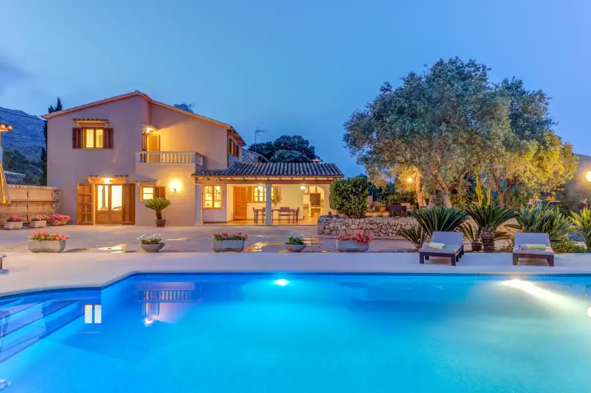 A swimming pool in front of a house, with loungers and trees nearby.