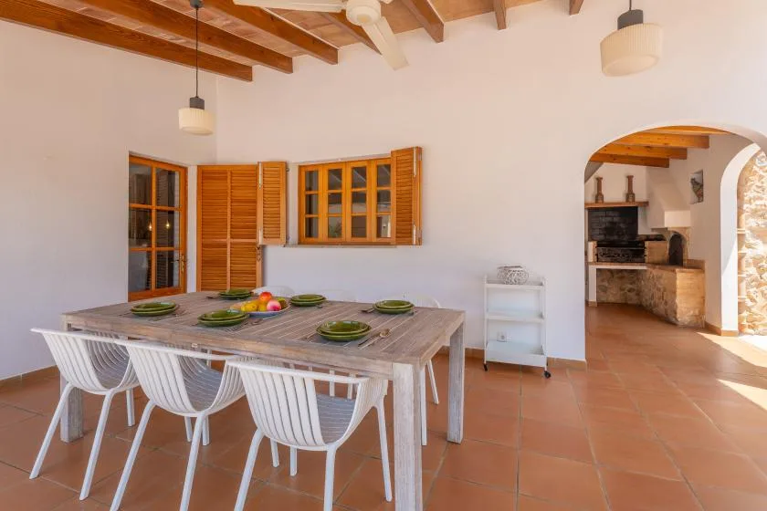 A dining area with a long table and white chairs beneath exposed wooden ceiling beams.