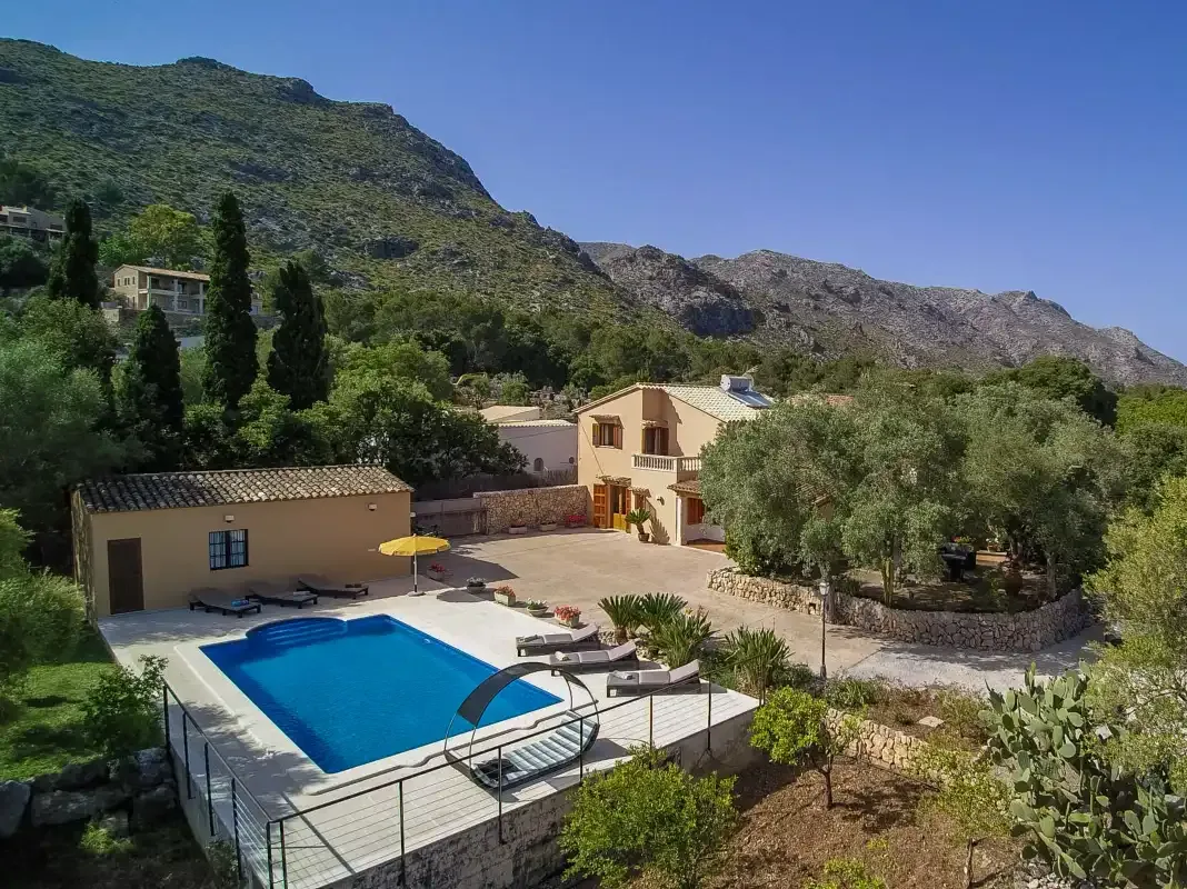A hillside house overlooks an outdoor swimming pool and surrounding mountain landscape.