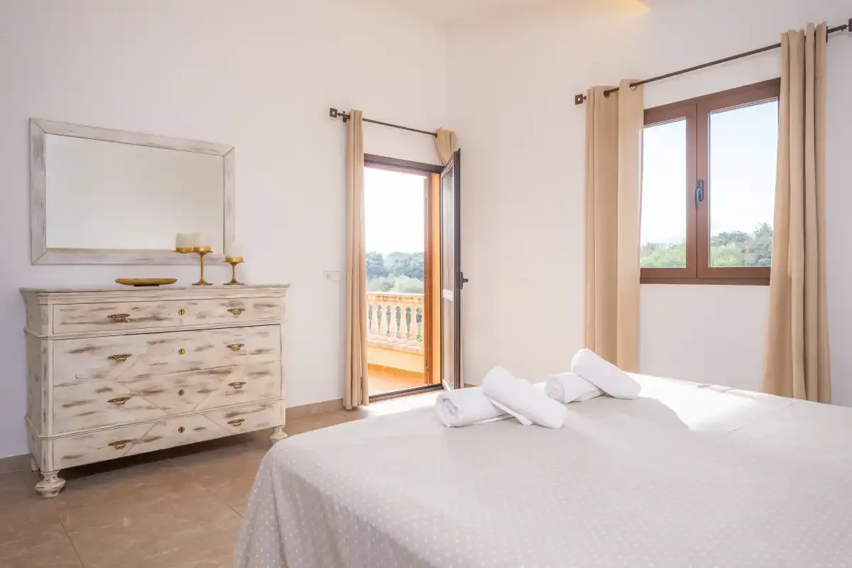 A bright bedroom with a neatly made bed and windows opening onto a balcony.