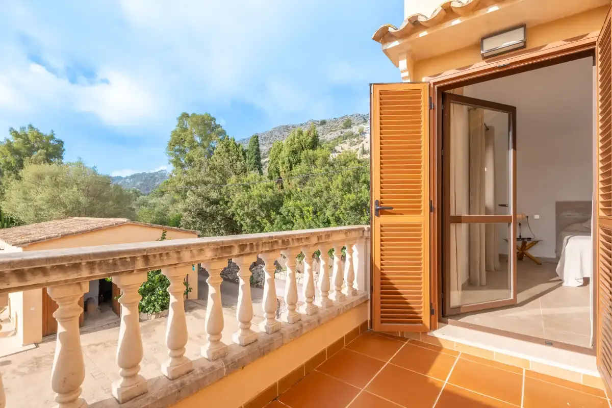 A sunny terrace overlooks trees and hills beside an open doorway.
