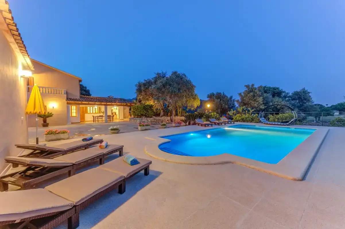 A swimming pool beside a paved patio with lounge seating at dusk.