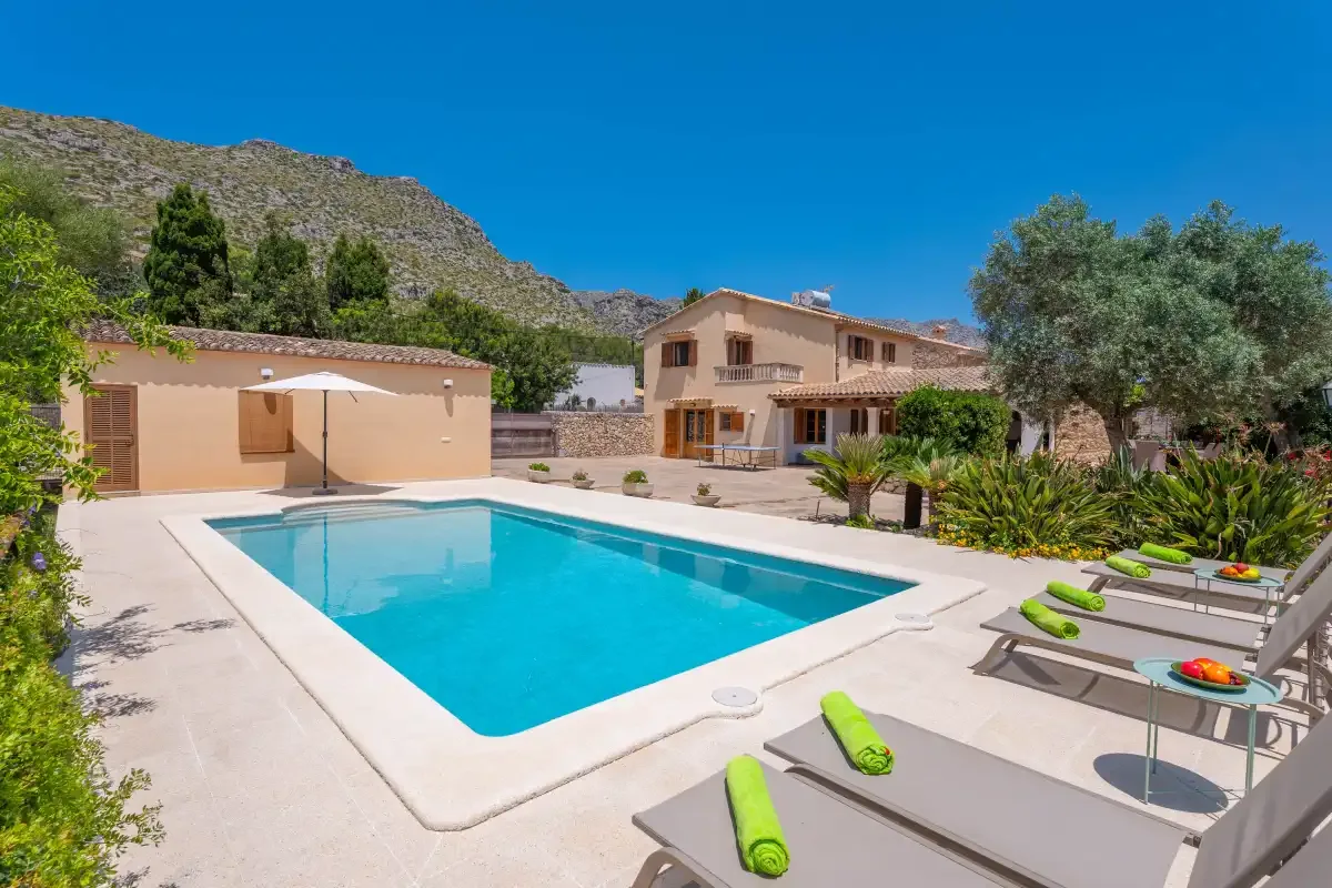 A swimming pool and lounge seating sit beside a house in a sunny outdoor courtyard.