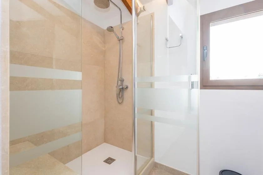 A bright bathroom shower with beige tiled walls and a frosted glass panel.