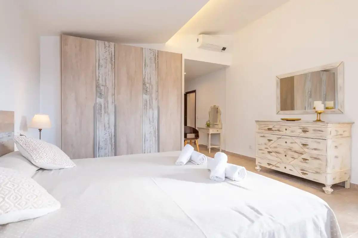 A bright bedroom with a large bed, wardrobe, and dresser.