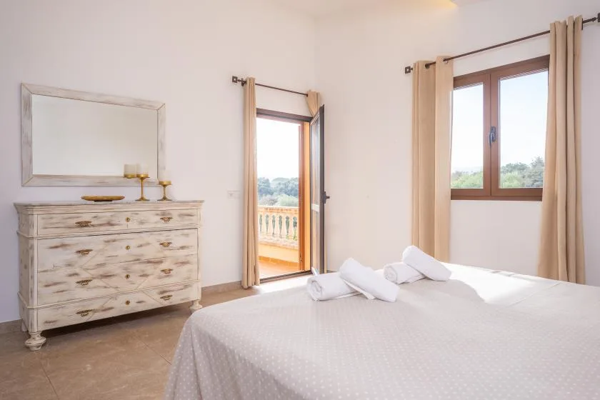 A bright bedroom with a neatly made bed and a window overlooking greenery.