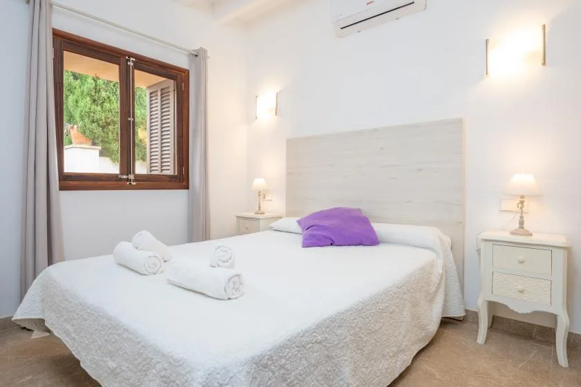 A bright bedroom with a neatly made bed and a window overlooking greenery.