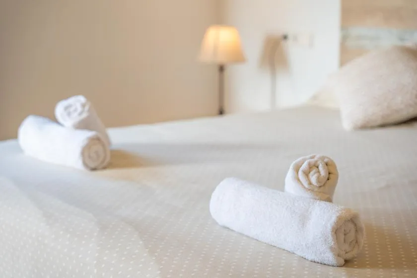 A neatly made bed with rolled white towels arranged on the bedding.